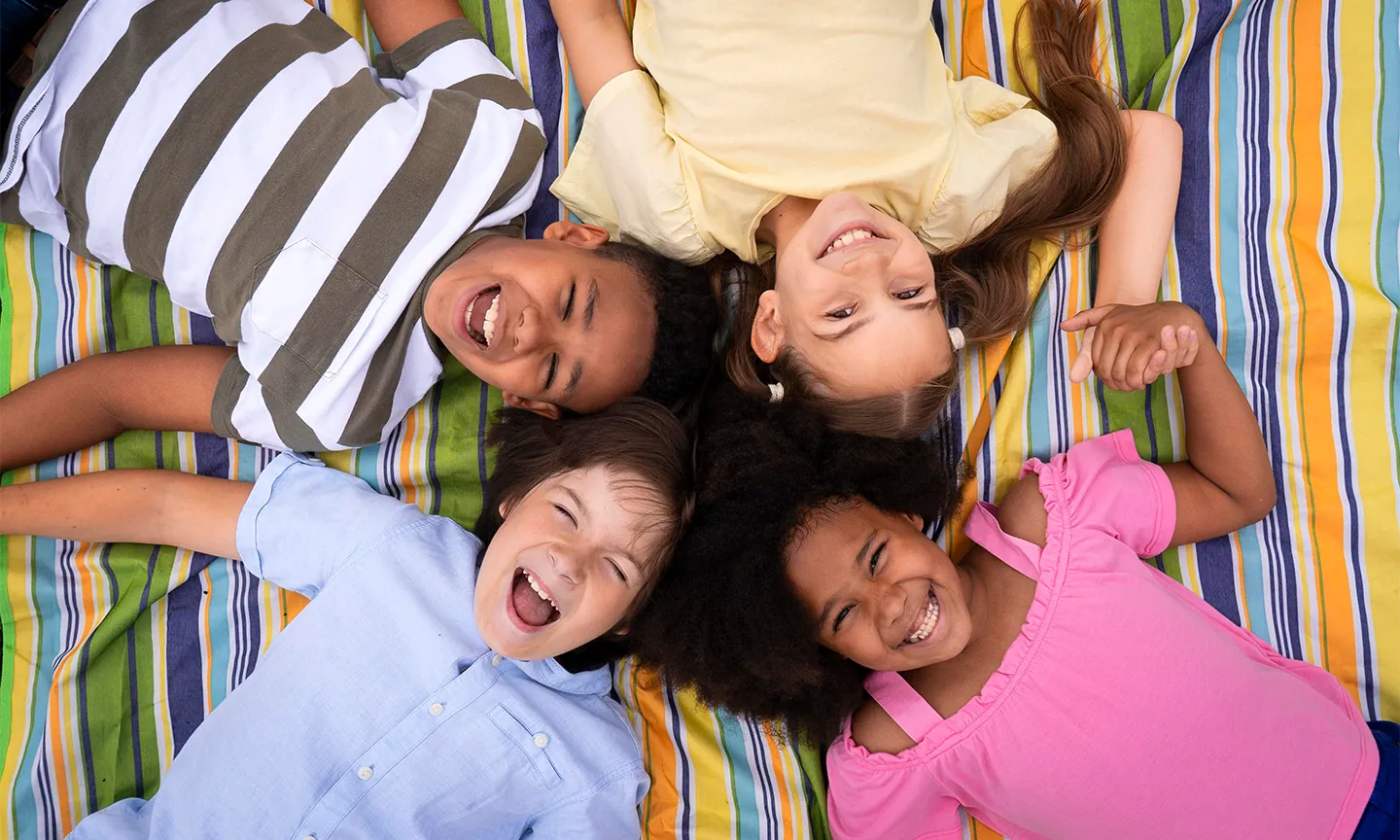 Vier lachende Kinder liegen im Kreis auf einer bunten Decke