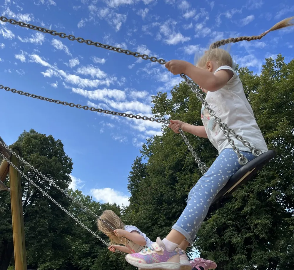 Zwei Kinder schaukeln unter blauem Himmel